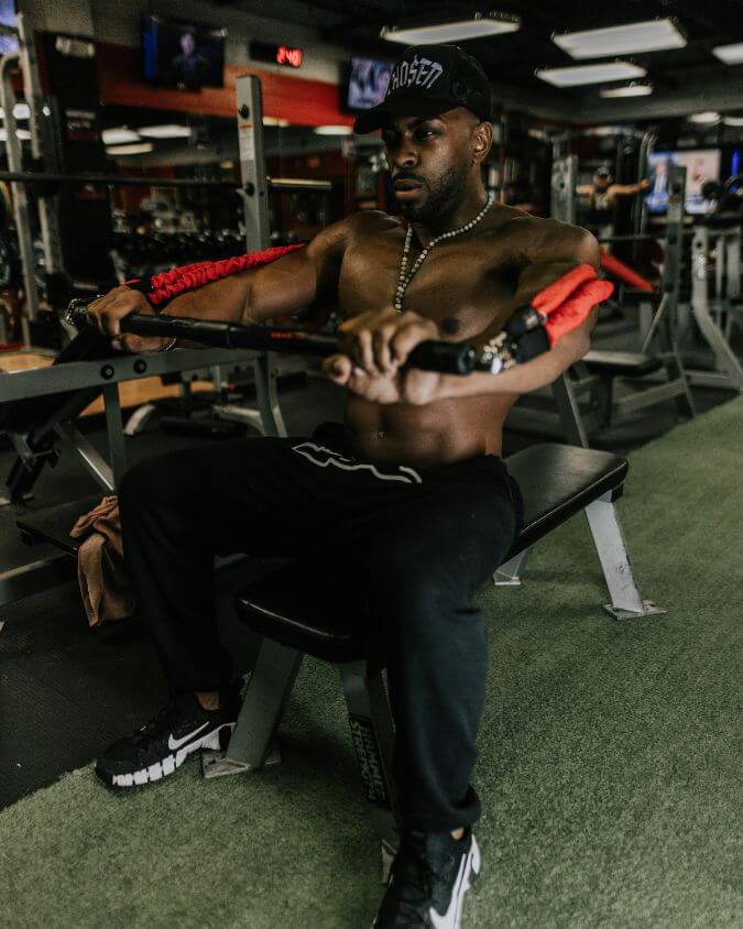 Man performing an chest press with a xbar fitness exercise bar using looped 50 pound red resistance bands and extension attachments creating 100 pounds of tension.