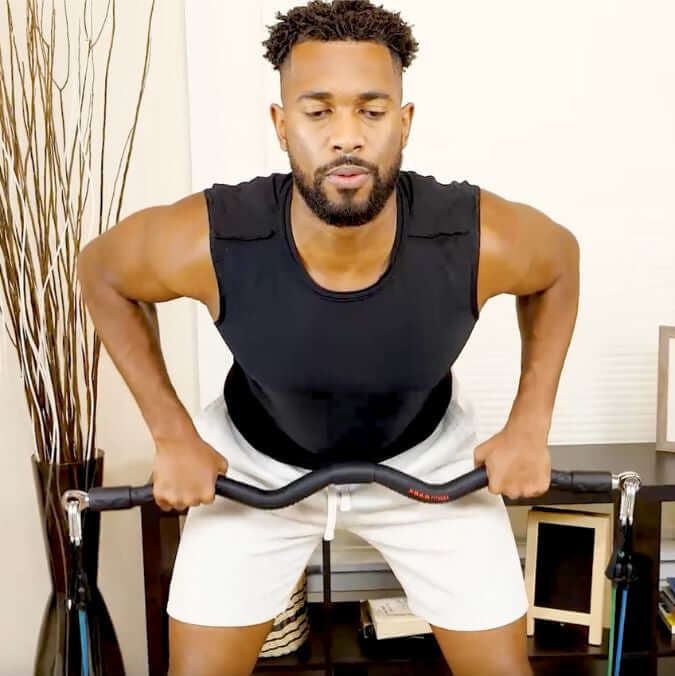 Man exercising inside home using medium resistance bands performing a function workout bent over row with a natural background.