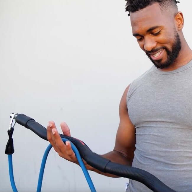 Man exercising outdoors holding xbar exercise bar with medium resistance bands with a natural background.