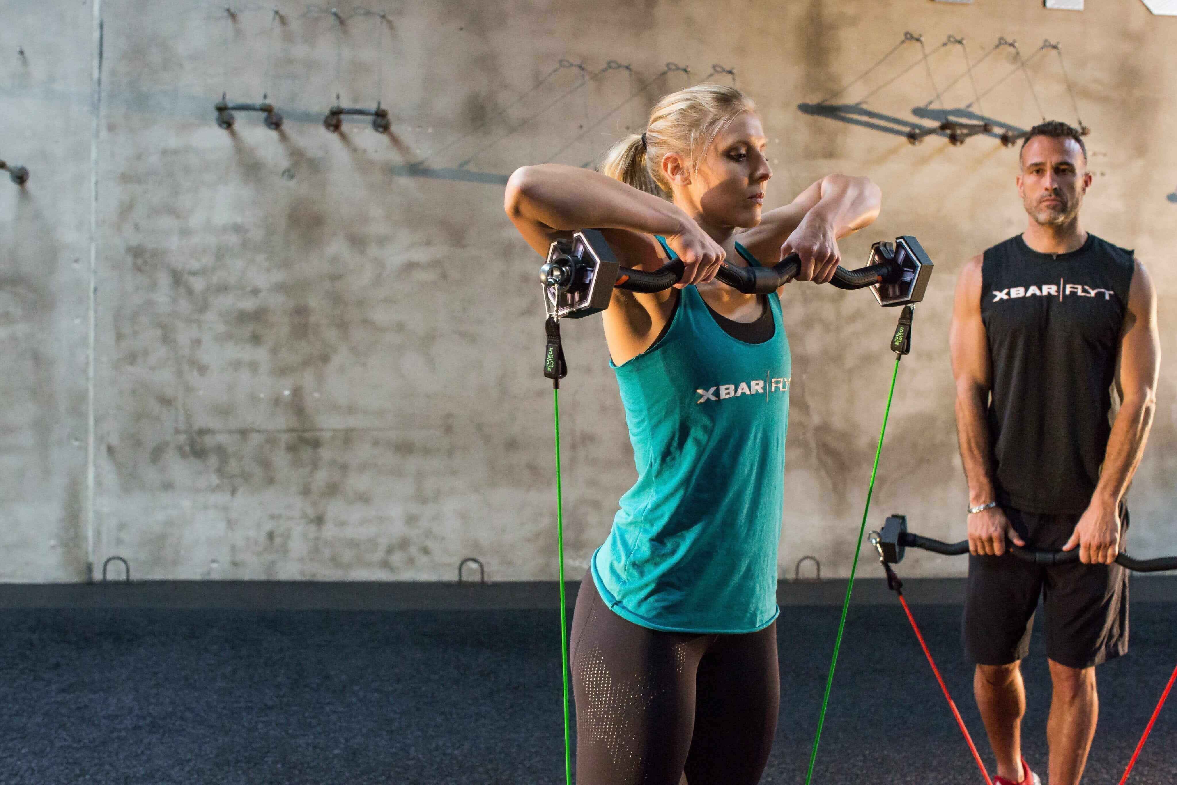 Woman performing Variable Resistance Training with resistance bands and weights in a gym setting.