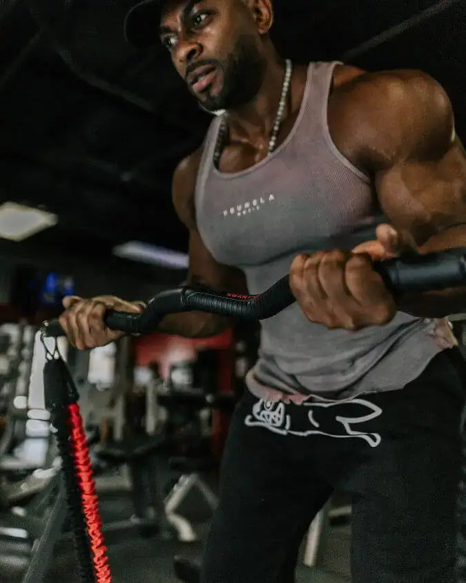 Man exercising with red and black resistance bands in a gym setting performing a bicep curl.