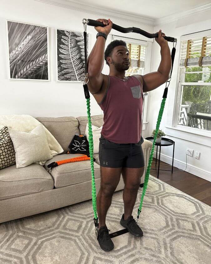 Man performing an overhead press with a xbar fitness exercise bar using 30 pound green resistance bands and extension attachments.