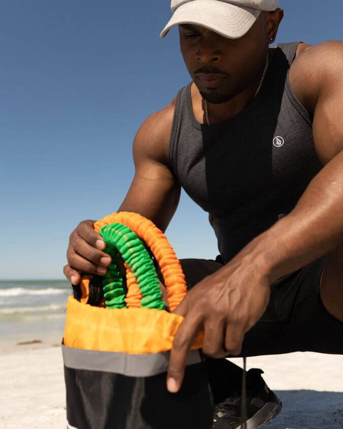 Man packing green and orange resistance bands in his travel accessory bag.