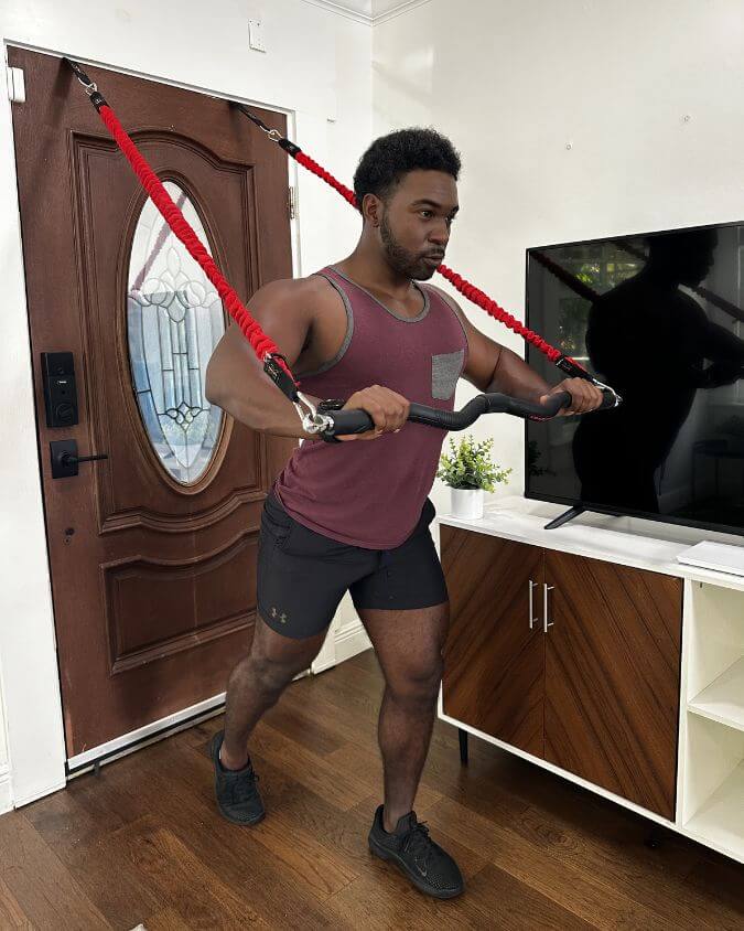 Man performing a chest press with a xbar fitness exercise bar using 50 pound red resistance bands and door anchor attachments in the home.