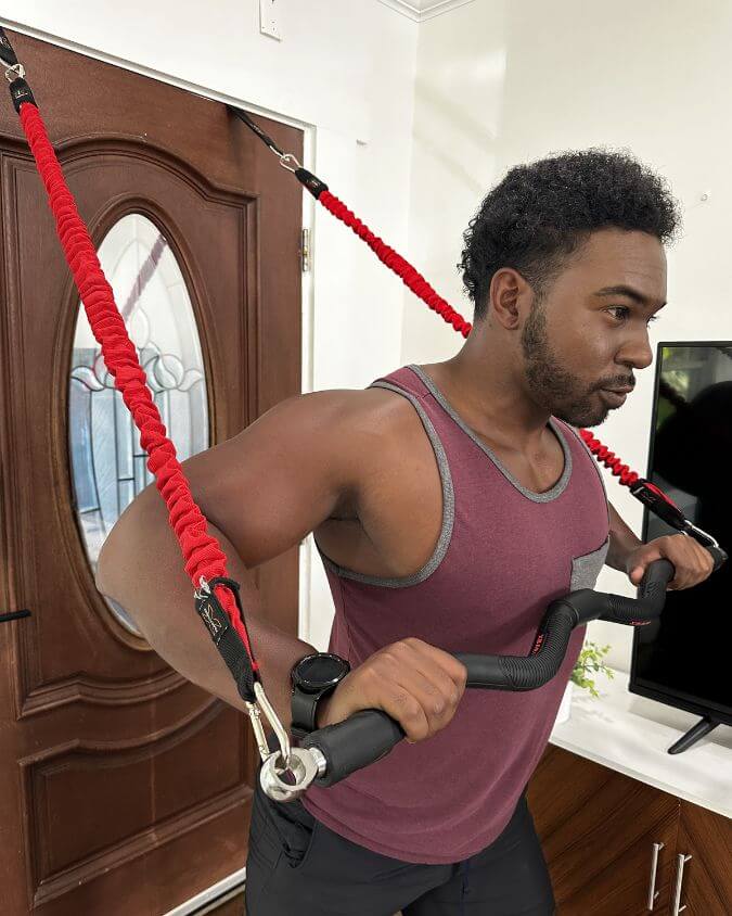Man performing a chest press with a xbar fitness exercise bar using 50 pound red resistance bands and door anchor attachments.