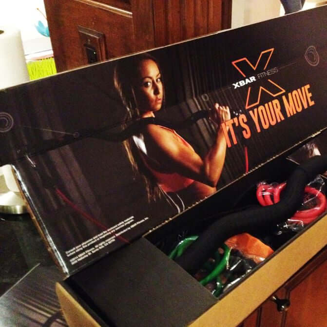 XBar Fitness product packaging with a woman and text 'It's Your Move' on a wooden surface.