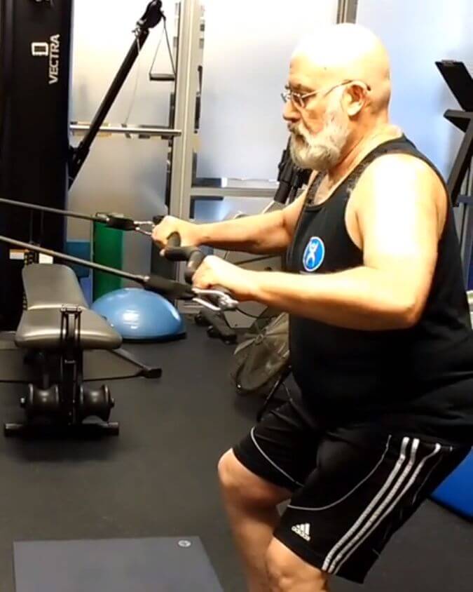 Man using xbar exercise bar with heavy resistance black band with 70lbs of tension inside performing a row to show you can workout and exercise anywhere.