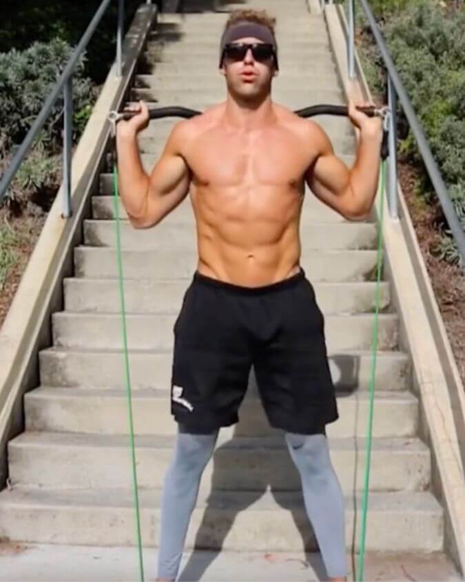 Main using green light resistance band performing a squats curl in a outside setting showing that you can workout with xbar fitness products anywhere.