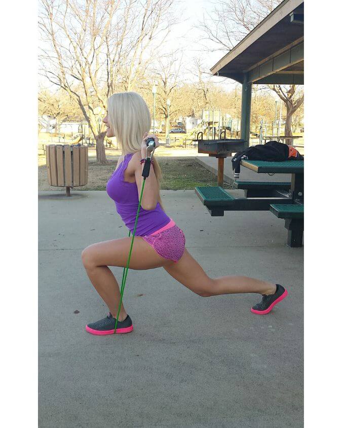 Woman using green light resistance band performing a lunge in a outside at a park showing that you can workout with xbar fitness products anywhere.