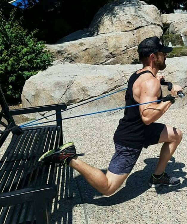 Man exercising outdoors using medium resistance bands performing a function workout lunge and chest press with a natural background.