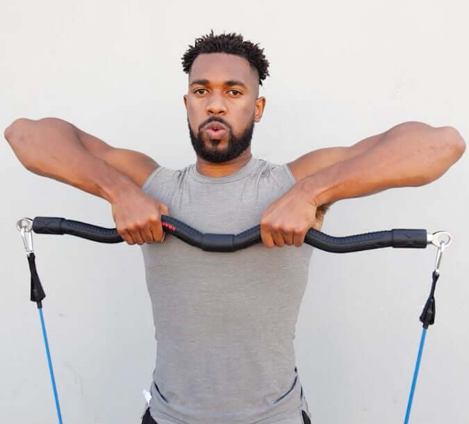Man exercising outdoors using medium resistance bands performing a function workout upright row with a natural background.