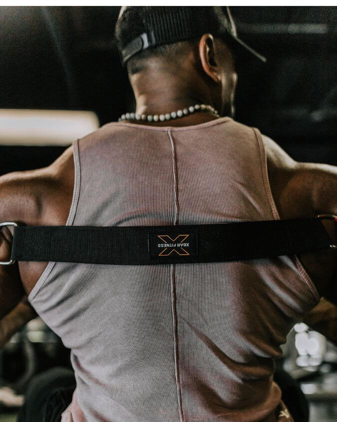 Person wearing a gray tank top with a black strap over shoulders, gym equipment in the background