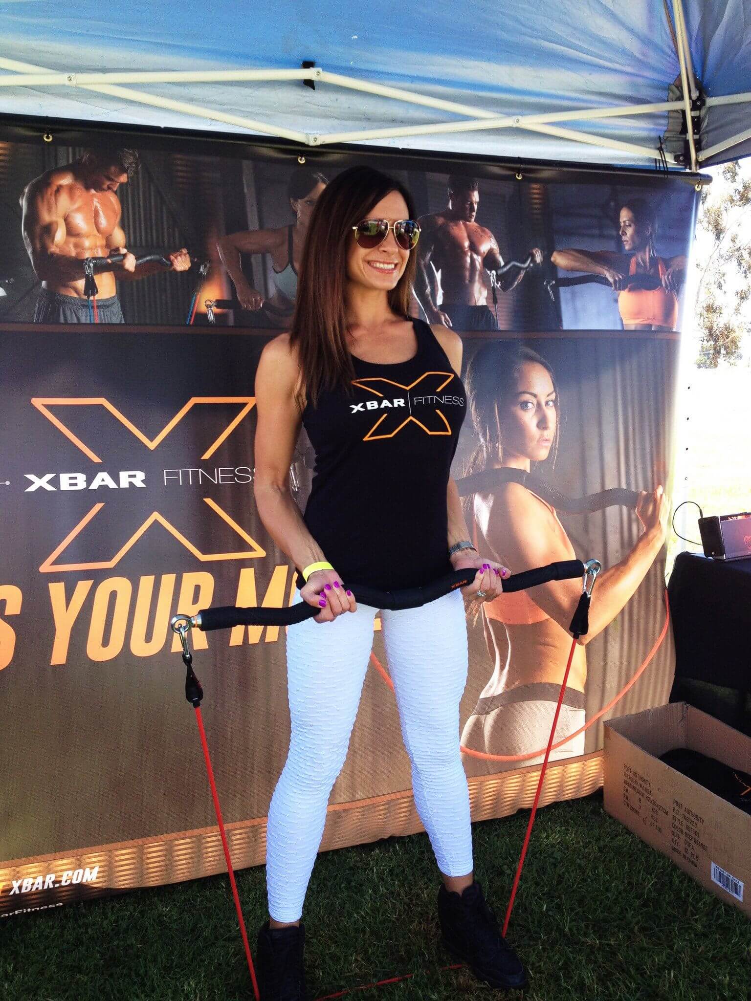 Woman modeling the Exercise Bar at an outdoor fitness event, showcasing its use and design.